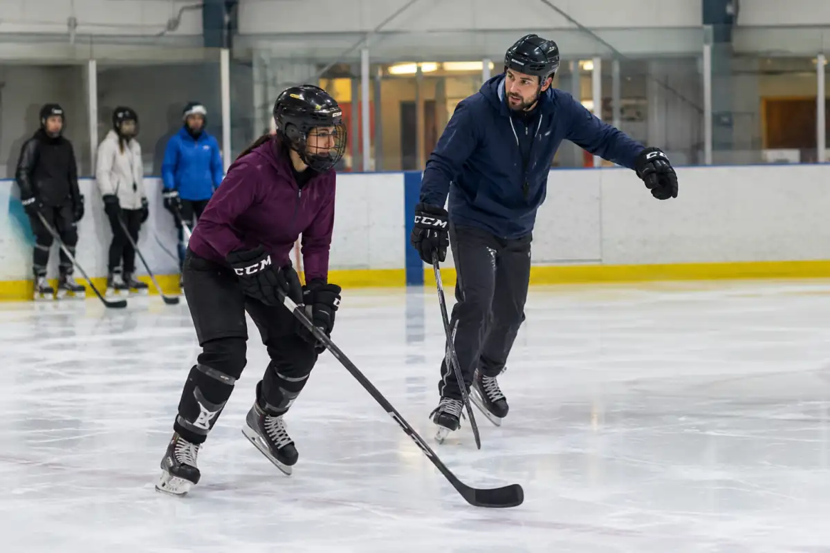 Un adulte débutant en équipement apprend à glisser sur la glace sous la supervision d’un entraîneur de hockey.