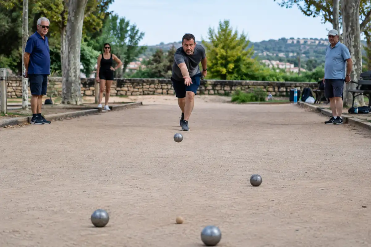 Un joueur prend son élan sur un terrain provençal et lance une boule métallique vers le but pendant une partie de jeu provençal.
