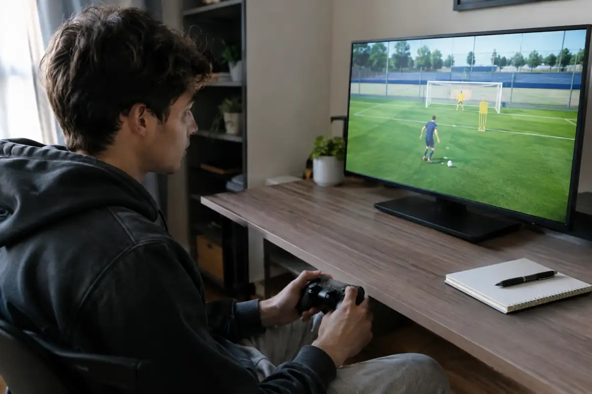 Joueur amateur d’e-football travaillant la finition sur un exercice en jeu et notant ses résultats pendant une séance d’entraînement.