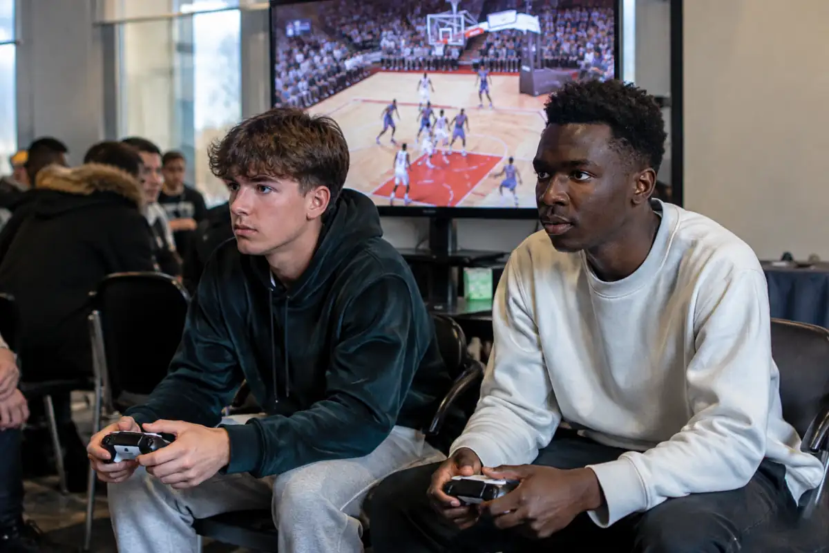 Deux joueurs disputent une partie de basket en jeu vidéo, manette en main, lors d’un match d’e-sport en salle.