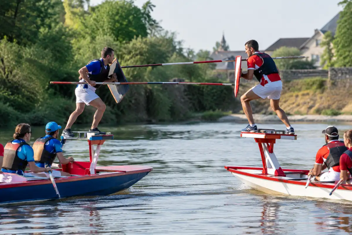 Jouteurs alsaciens en équilibre sur leurs embarcations, lance et bouclier en main lors d’un passage sur l’eau.