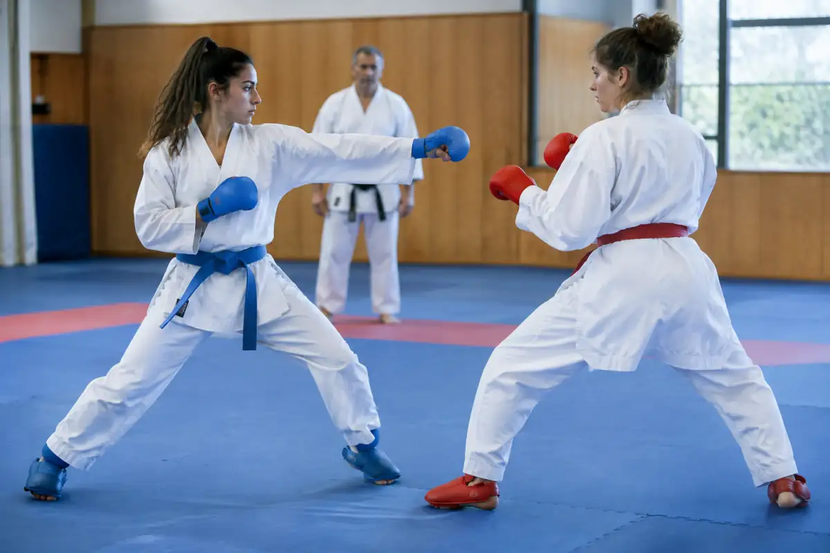 Deux karatékas en kimono travaillent un kumite contrôlé sur tatami dans un dojo, avec protections et garde adaptée.