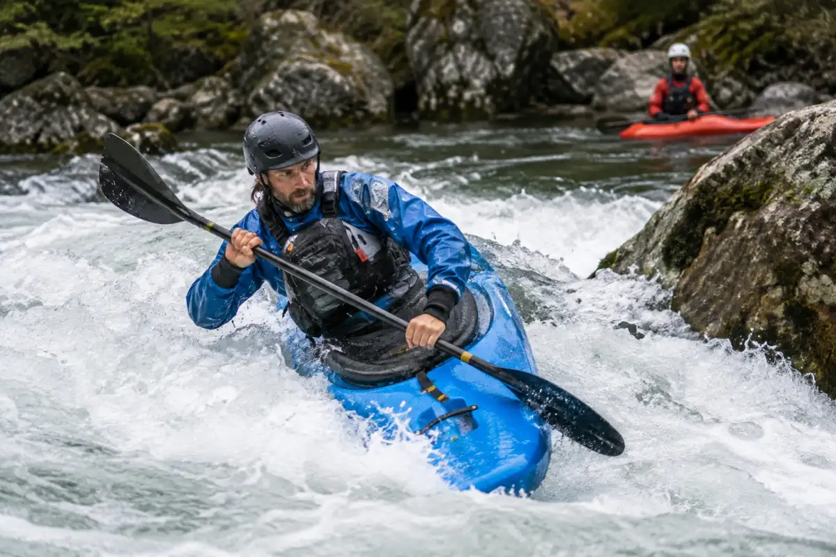 Kayakiste en équipement d’eau vive négociant un rapide rocheux lors d’une descente de kayak extrême en montagne.