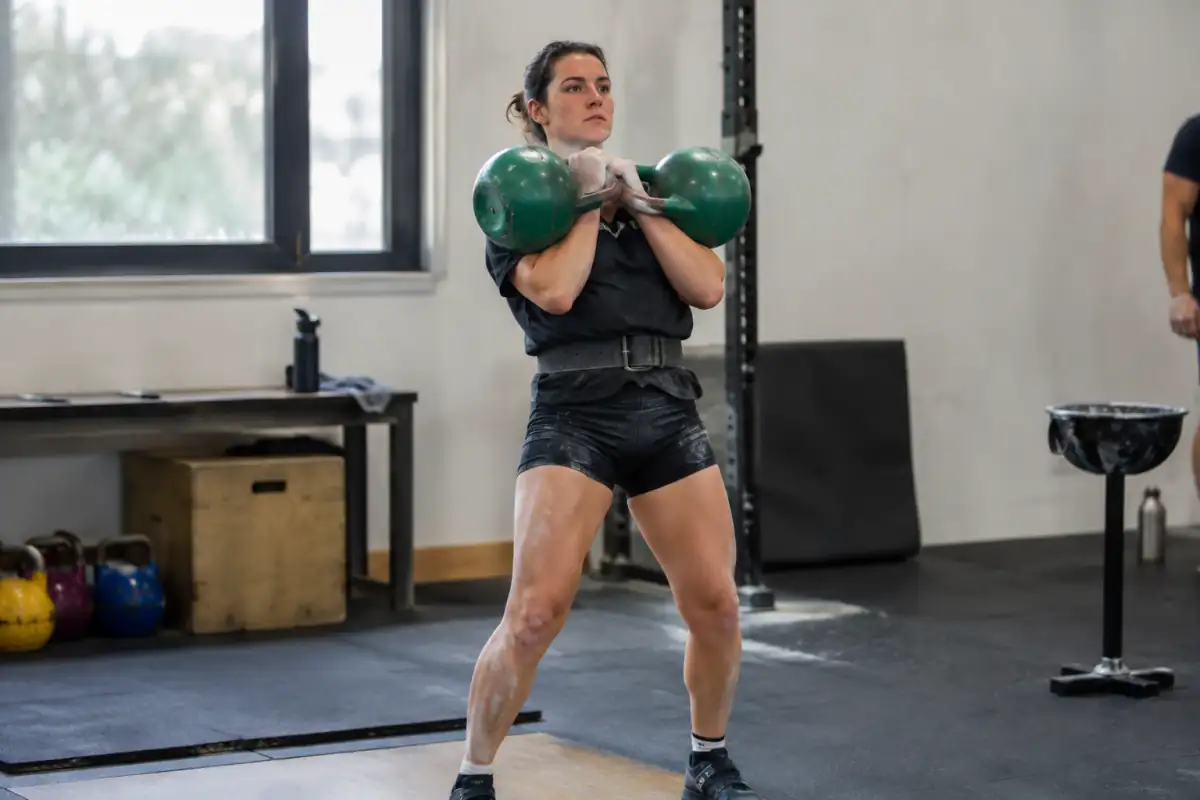 Athlète réalisant un jerk avec deux kettlebells de compétition lors d’un entraînement de kettlebell sport en salle.
