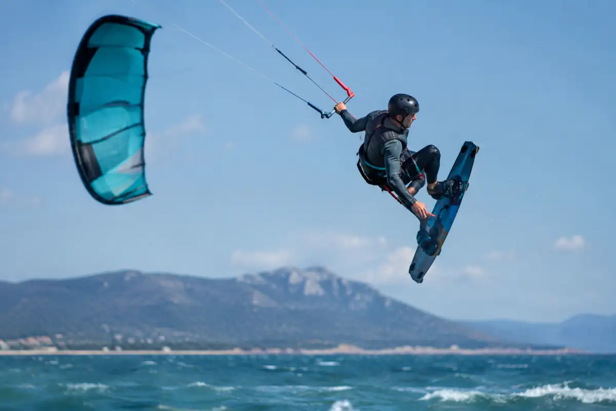 Un kitesurfeur en combinaison réalise un saut freestyle avec une planche twintip au-dessus de l’eau.