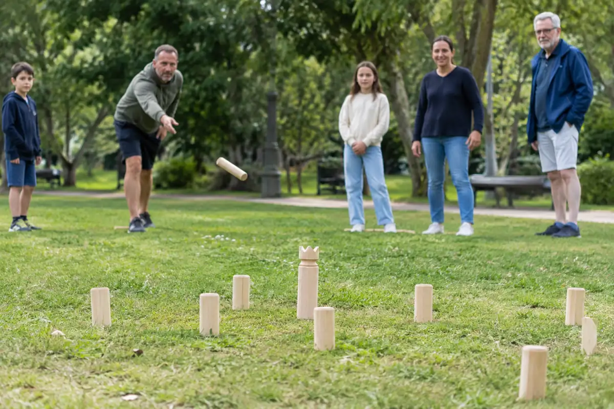 Partie de kubb en extérieur : une joueuse lance un bâton en bois vers les kubbs adverses sur un terrain herbeux.
