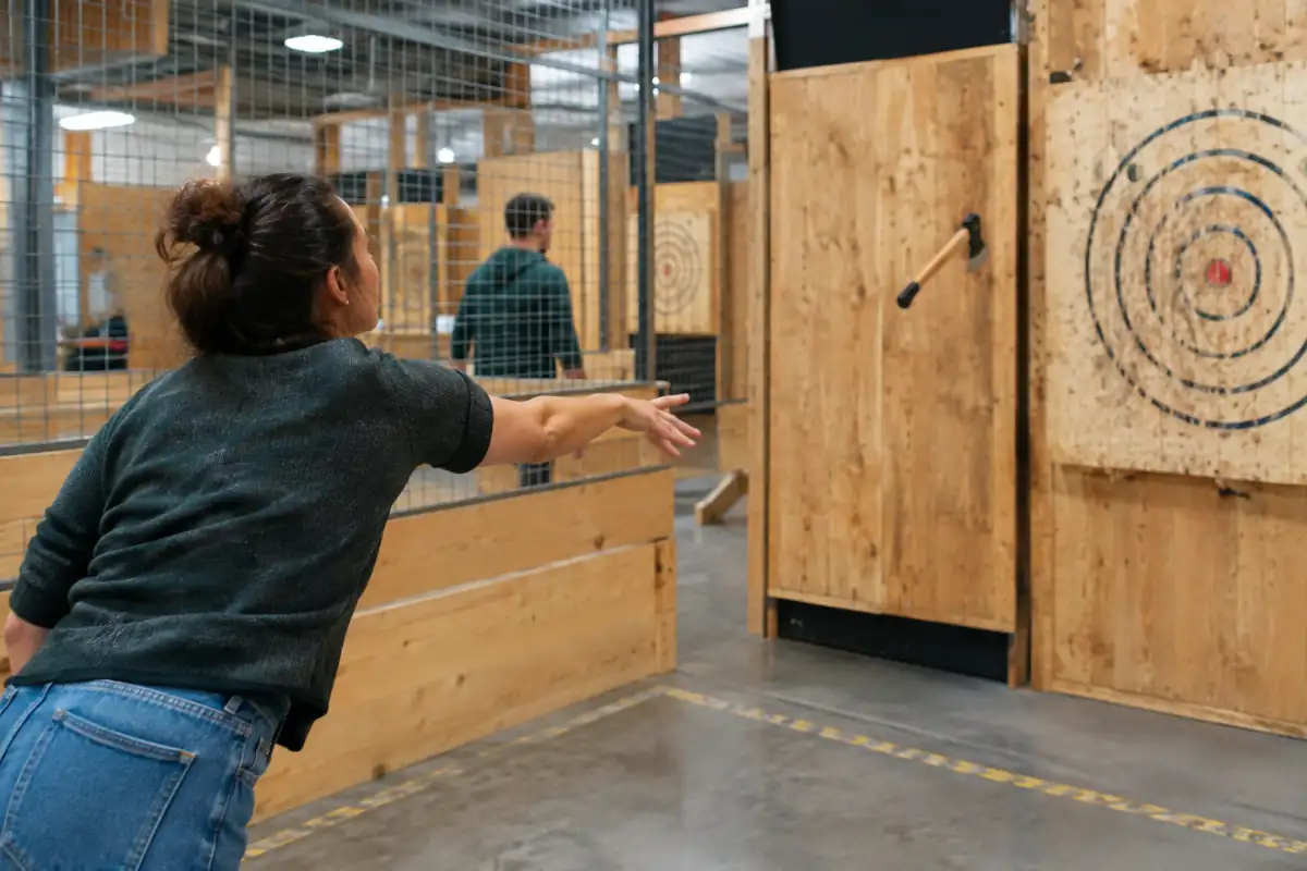 Un pratiquant lance une hache vers une cible en bois dans une piste intérieure aménagée et encadrée.
