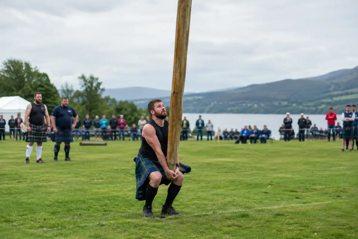 Un athlète redresse un caber avant son lancer sur une aire en herbe lors d’un rassemblement de jeux écossais.