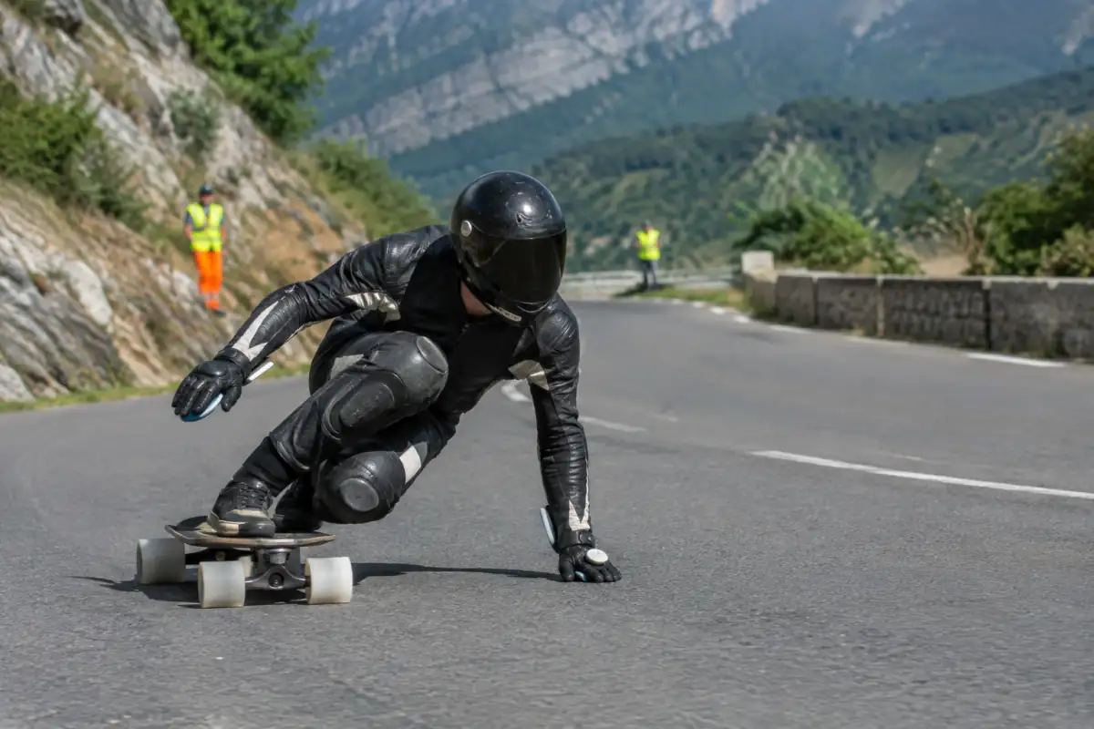 Pilote de longboard downhill en casque intégral et combinaison, négociant un virage sur une route fermée.