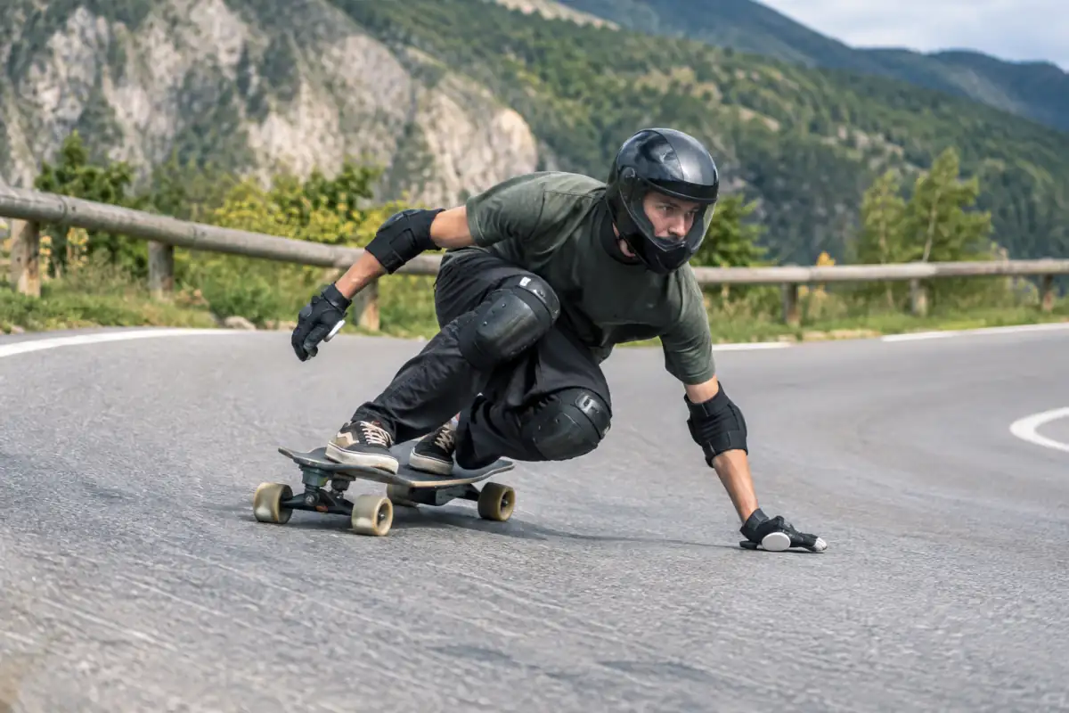 Un pratiquant de longboard en casque intégral réalise un dérapage contrôlé sur une route fermée à la circulation.