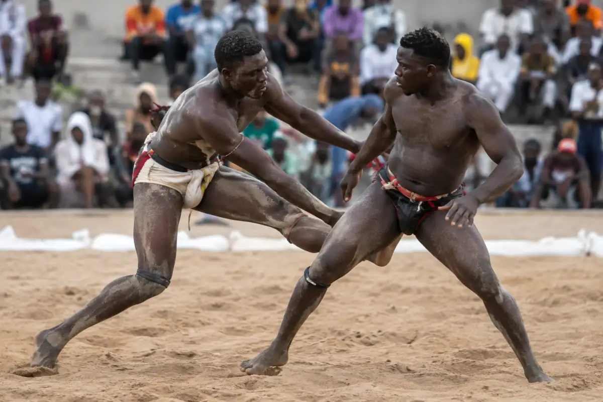 Deux lutteurs sénégalais en tenue traditionnelle cherchent à se déséquilibrer dans une arène de sable lors d’un combat de laamb.
