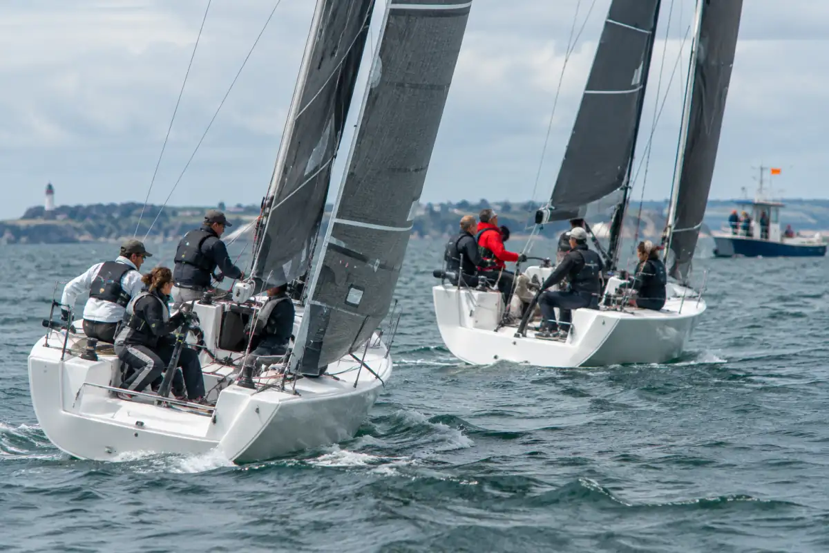 Deux équipages s’affrontent sur des voiliers identiques lors d’un match racing à la voile, au large de la côte française.