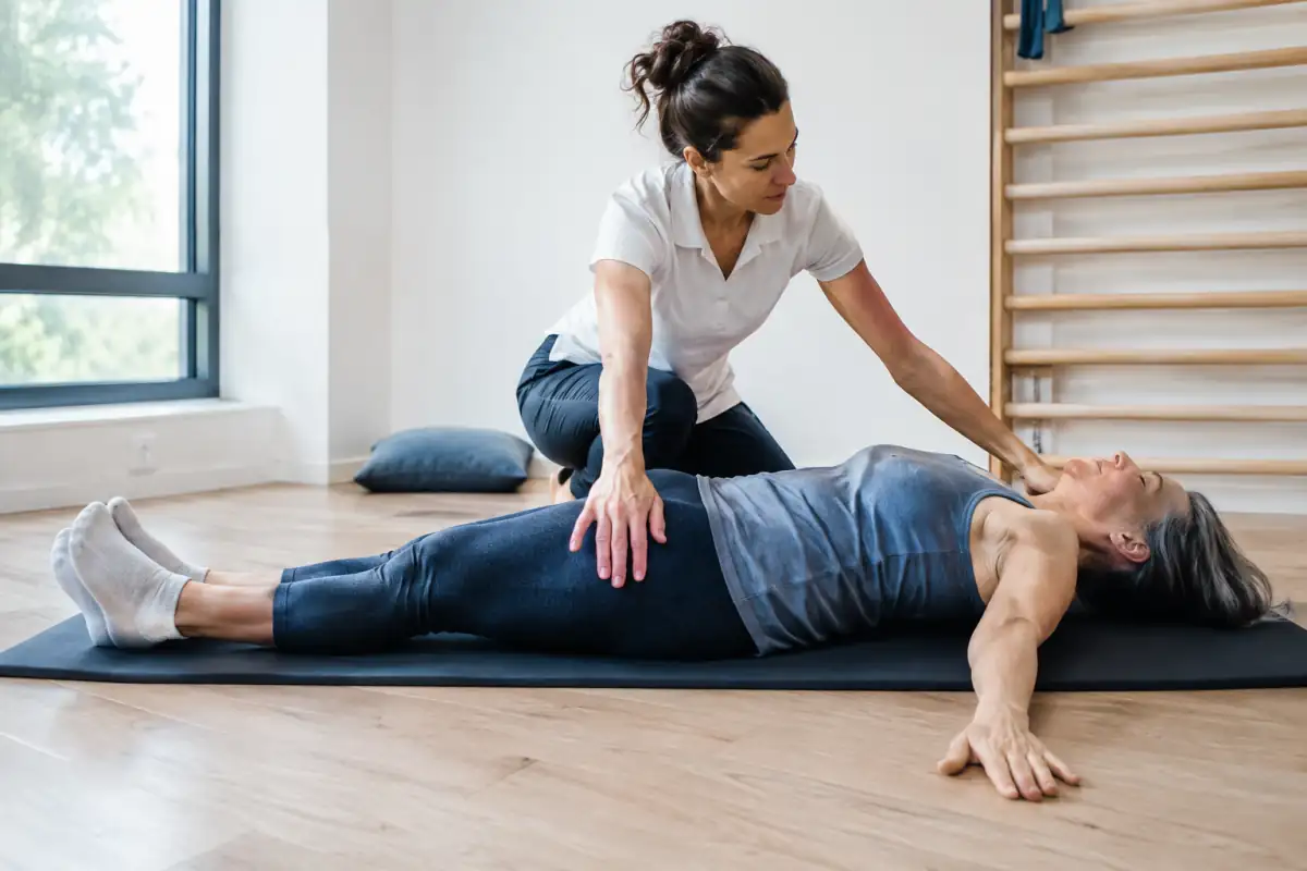 Séance de méthode Mézières : un kinésithérapeute accompagne une personne dans une posture d’étirement au sol.
