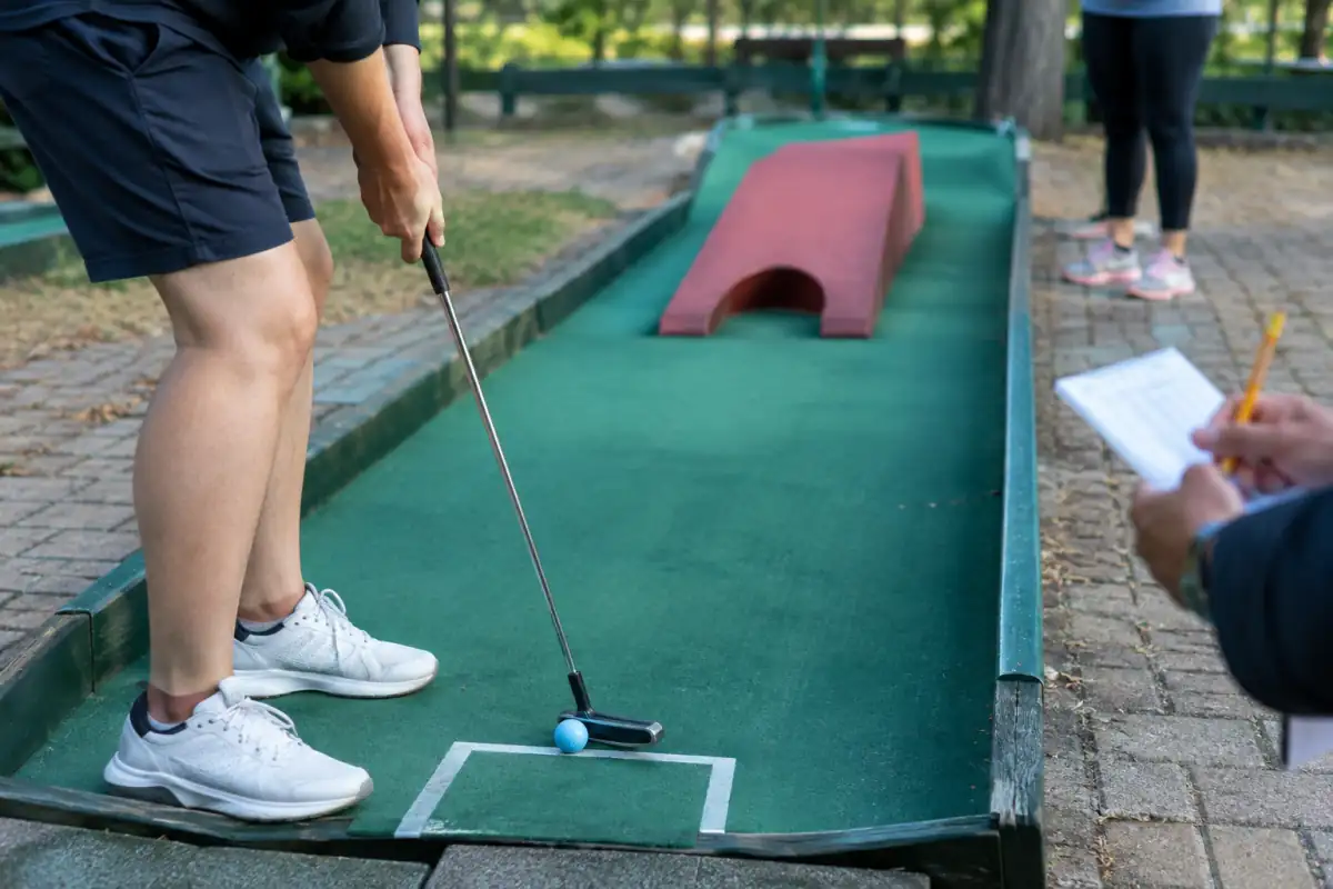 Joueur de mini-golf plaçant sa balle dans la zone de départ, près d’une ligne de passage et d’un obstacle.