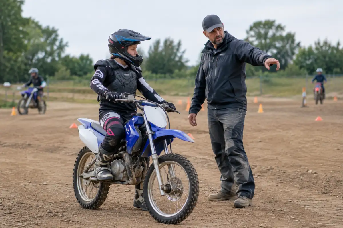 Un moniteur accompagne un débutant à moto sur une zone d’apprentissage plane d’un club de motocross.