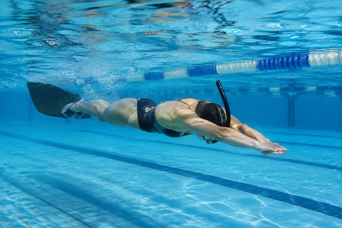 Nageuse en monopalme et tuba frontal avançant en ondulation dans un couloir de piscine pendant un entraînement.