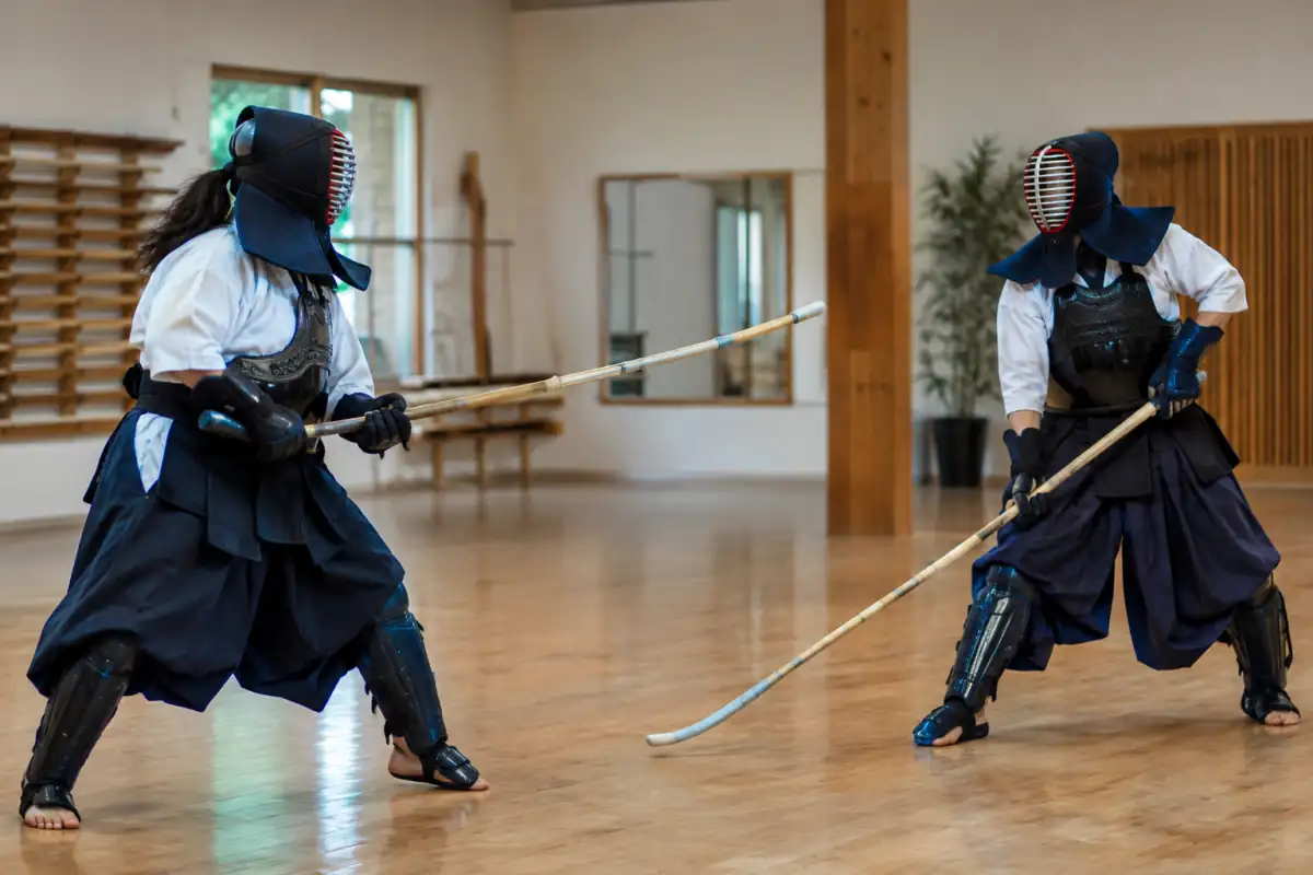 Deux pratiquants de naginata en armure exécutent une frappe contrôlée avec leur arme en bambou dans un dojo.