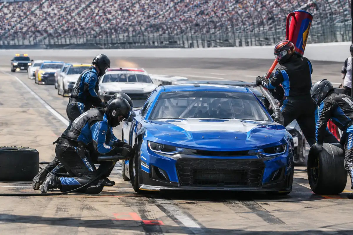 Équipe NASCAR changeant les pneus d’une voiture immobilisée dans son emplacement pendant un arrêt aux stands sous neutralisation.