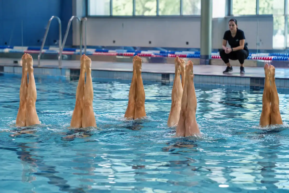 Nageuses artistiques en entraînement dans un bassin, jambes verticales hors de l’eau et alignées en formation.