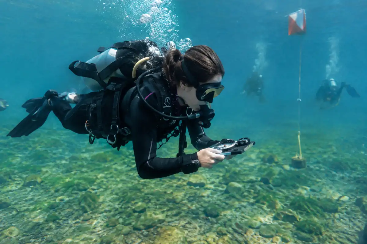 Une athlète équipée d’une bouteille, d’une boussole et d’un compteur suit un parcours d’orientation subaquatique dans un lac.