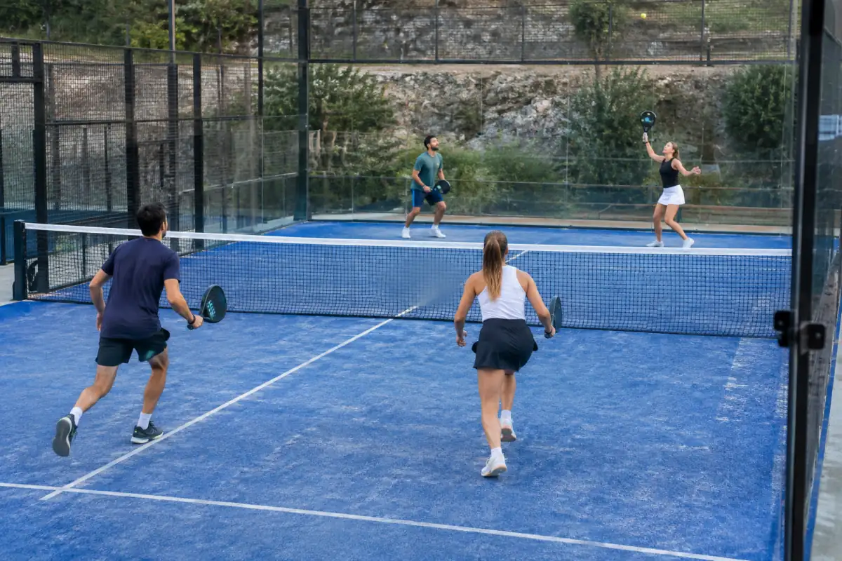 En double au padel, deux partenaires avancent ensemble après un lob tandis que leurs adversaires reculent pour défendre.