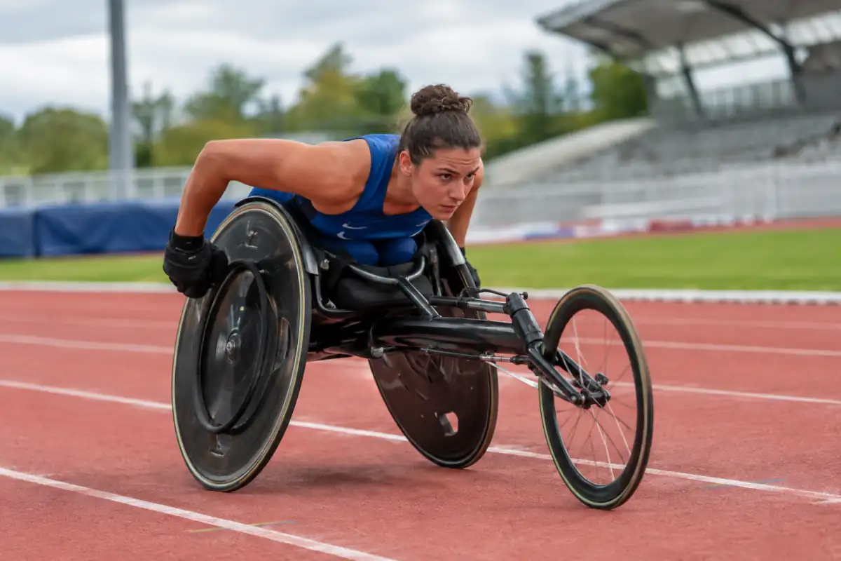 Un athlète propulse son fauteuil de course sur la piste lors d’une épreuve de para-athlétisme en stade.