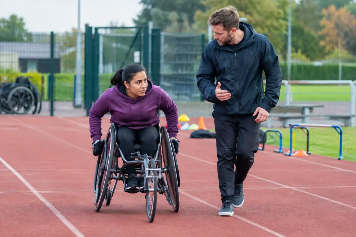 Une personne en fauteuil roulant découvre une poussée contrôlée sur une piste, accompagnée par un entraîneur de club.