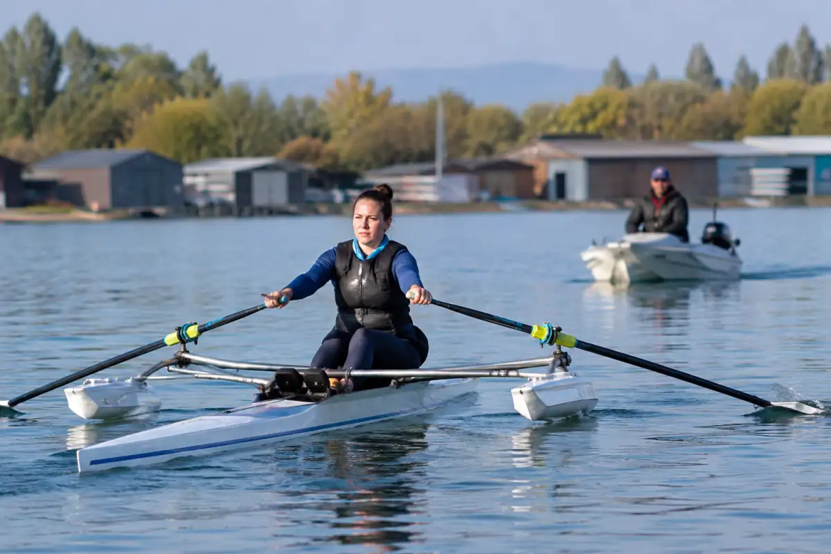 Un rameur en para-aviron propulse un skiff équipé de flotteurs stabilisateurs sur un plan d’eau calme.