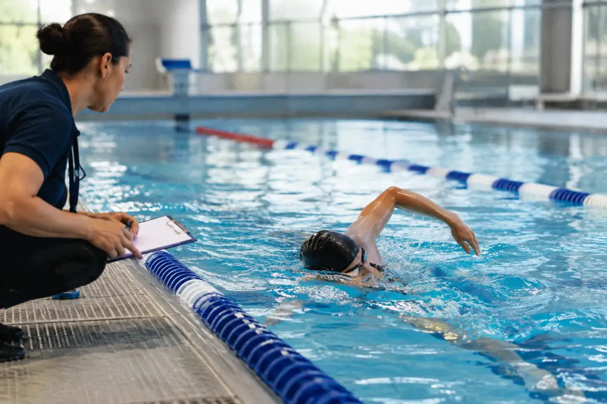 Un nageur réalise un mouvement de crawl dans un bassin tandis qu’un classificateur observe sa position et sa coordination.