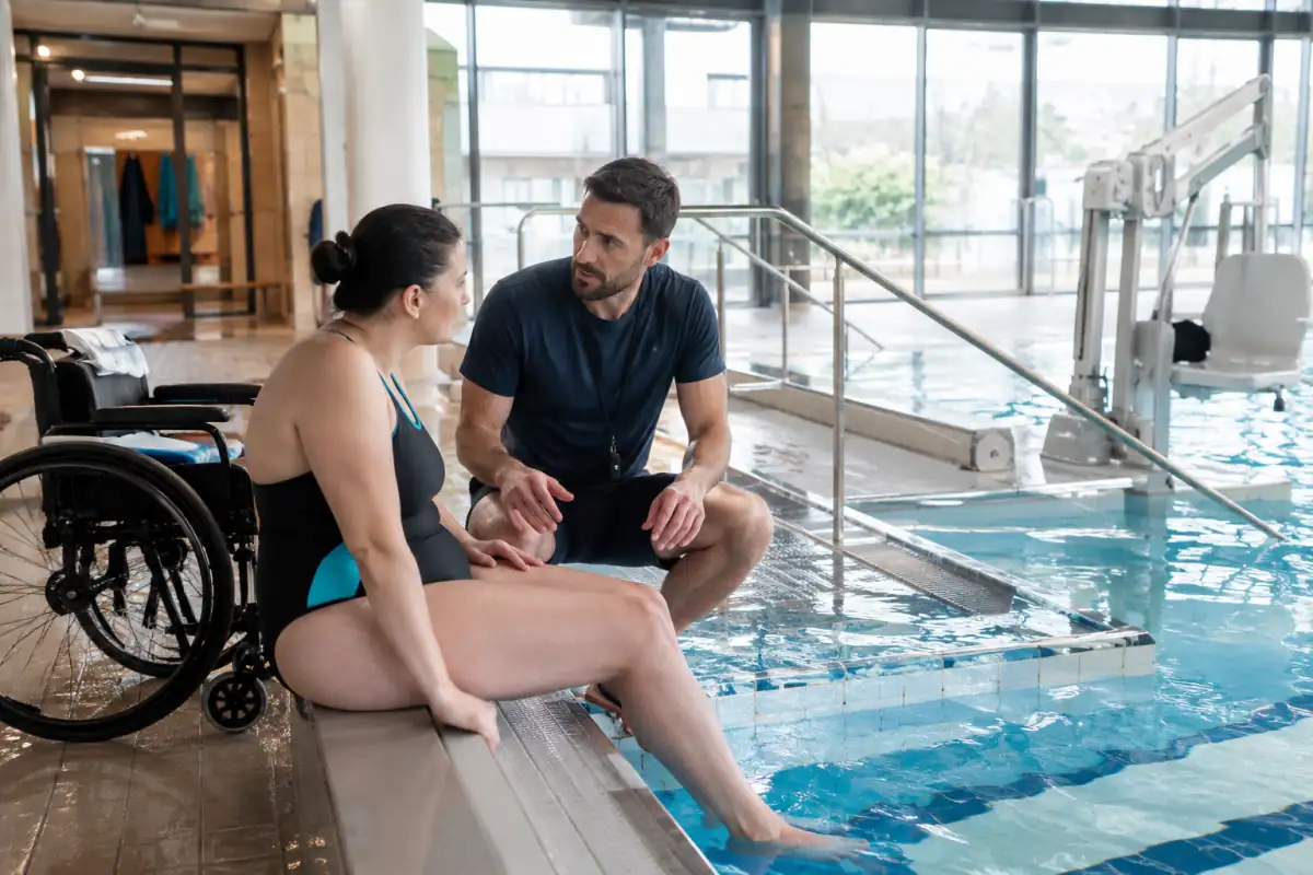 Un éducateur prépare une séance d’essai de para-natation avec une nageuse en fauteuil près d’un accès adapté au bassin.