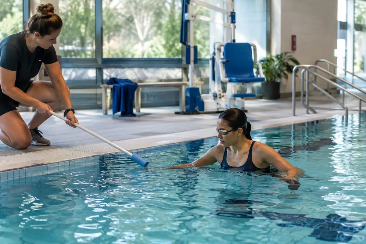 Nageur en lunettes dans une piscine accessible, accompagné d’un tapper équipé d’une perche à embout souple.