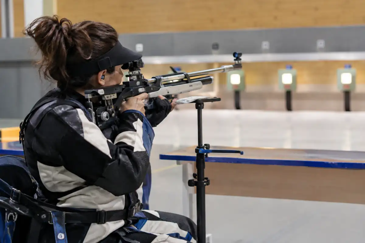 Athlète de para-tir sportif en position assise, visant une cible à 10 mètres avec une carabine à air comprimé.