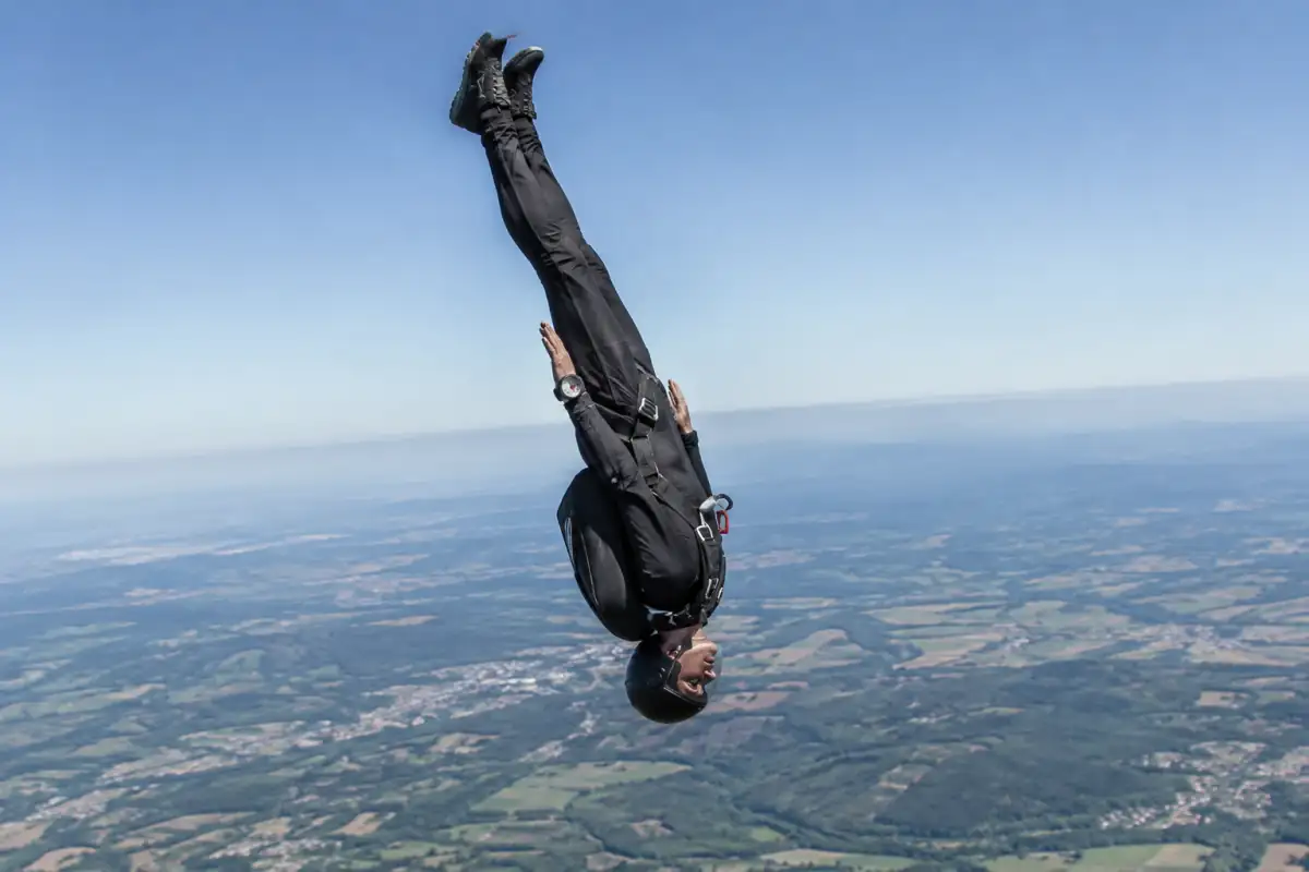 Un parachutiste en posture tête en bas pendant une épreuve de parachutisme de vitesse, équipé d’un casque et d’un parachute.
