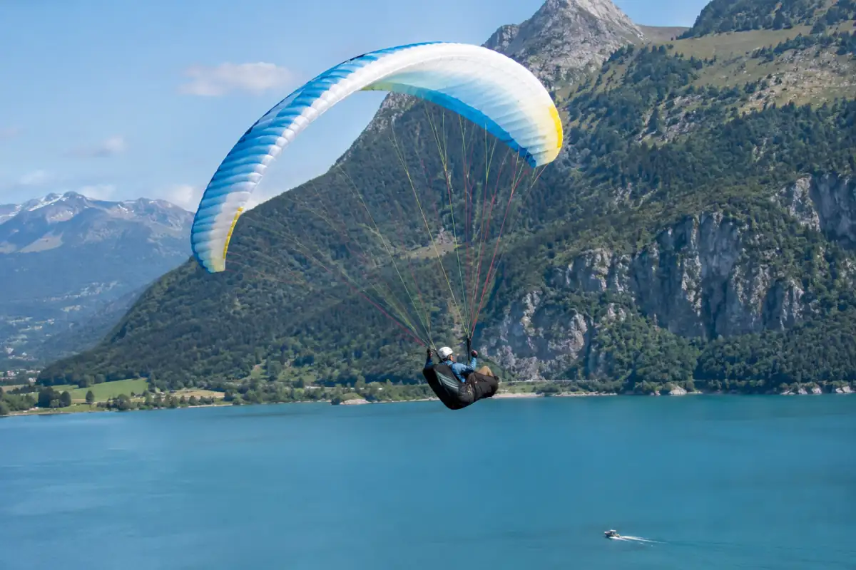 Un pilote exécute un wing-over en parapente acrobatique au-dessus d’un lac des Alpes, avec son équipement de sécurité.
