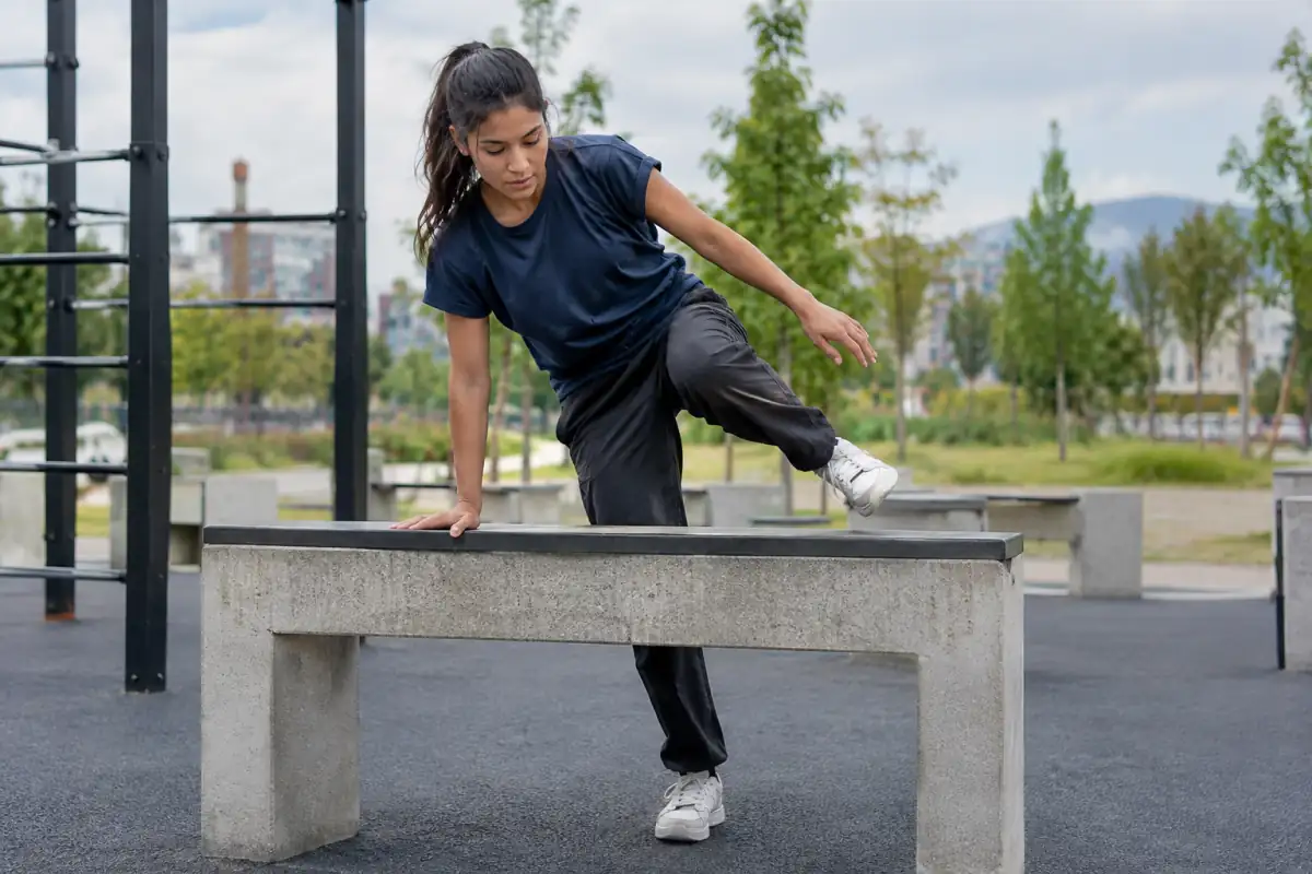Débutant en parkour qui apprend un passement de sécurité sur une barrière basse et stable, dans une zone de réception dégagée.