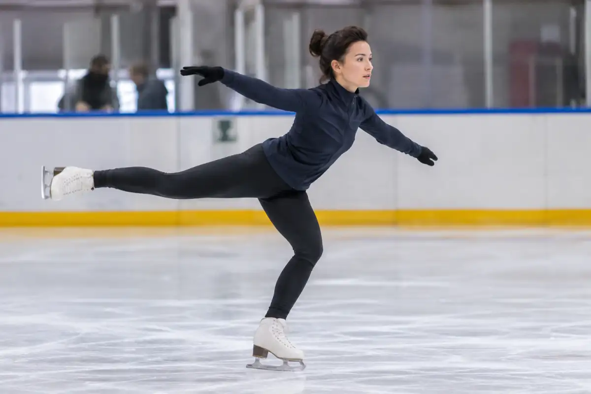 Patineuse artistique en tenue d’entraînement, genou fléchi à la réception d’un saut sur la glace.