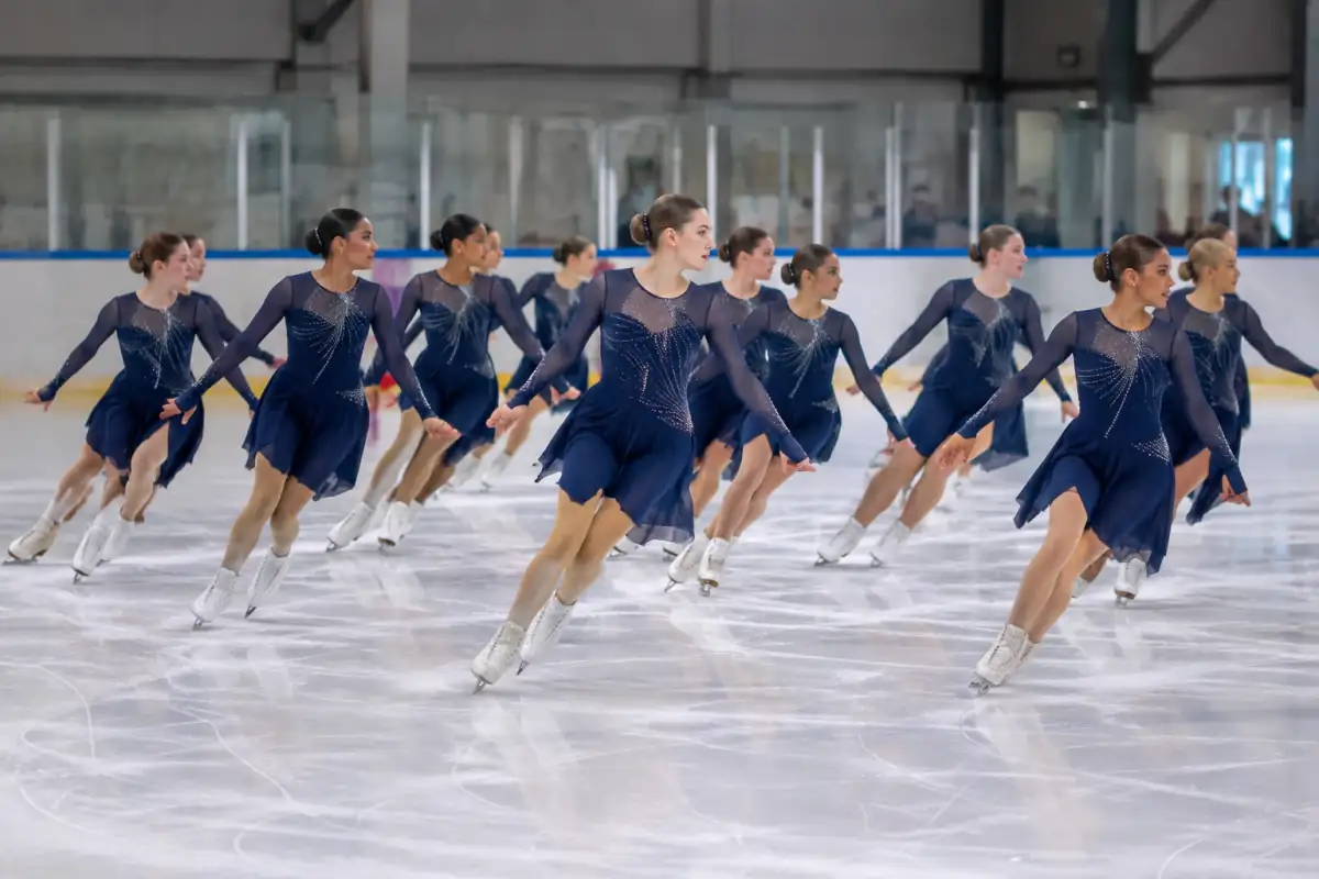 Équipe de patinage synchronisé réalisant une intersection en lignes croisées sur la glace d’une patinoire.