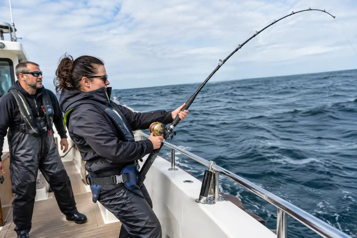 Pêcheur équipé d’un harnais combattant un poisson au large depuis un bateau de pêche en mer.