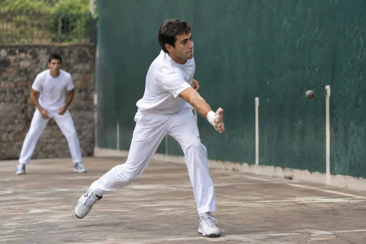 Joueur de pelote basque à main nue frappant une pelote contre le fronton, main protégée par des bandes adhésives.