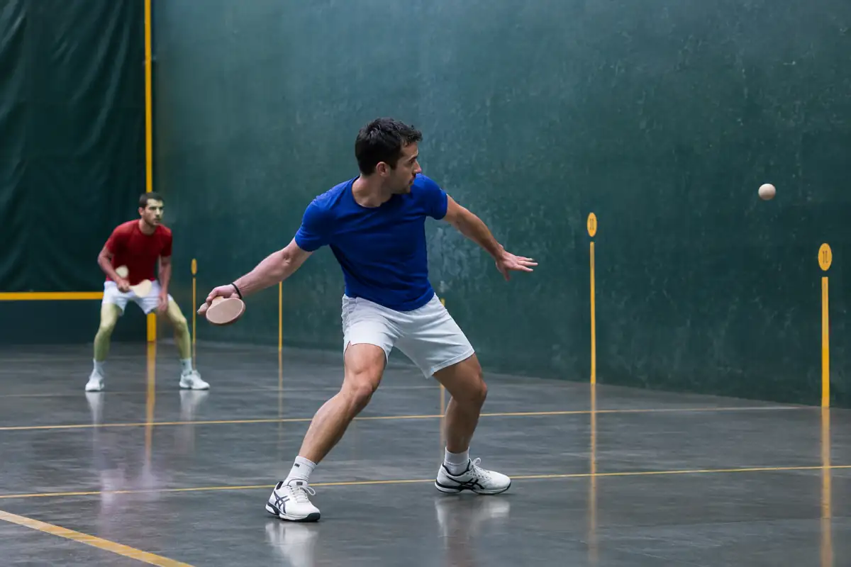 Joueur de pelote basque prêt à renvoyer la balle dans un fronton, avec les lignes du terrain visibles pour comprendre l’échange.