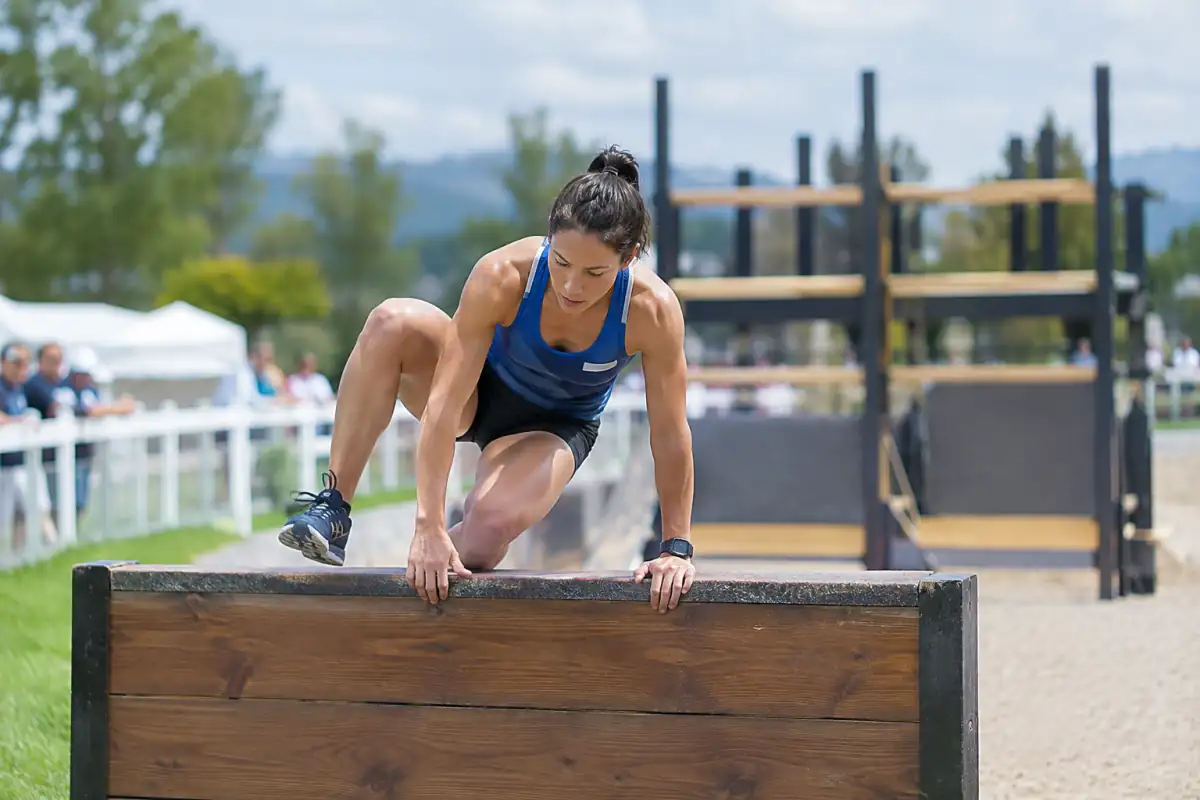Une athlète franchit un obstacle sur un parcours de pentathlon moderne, dans une compétition en extérieur.