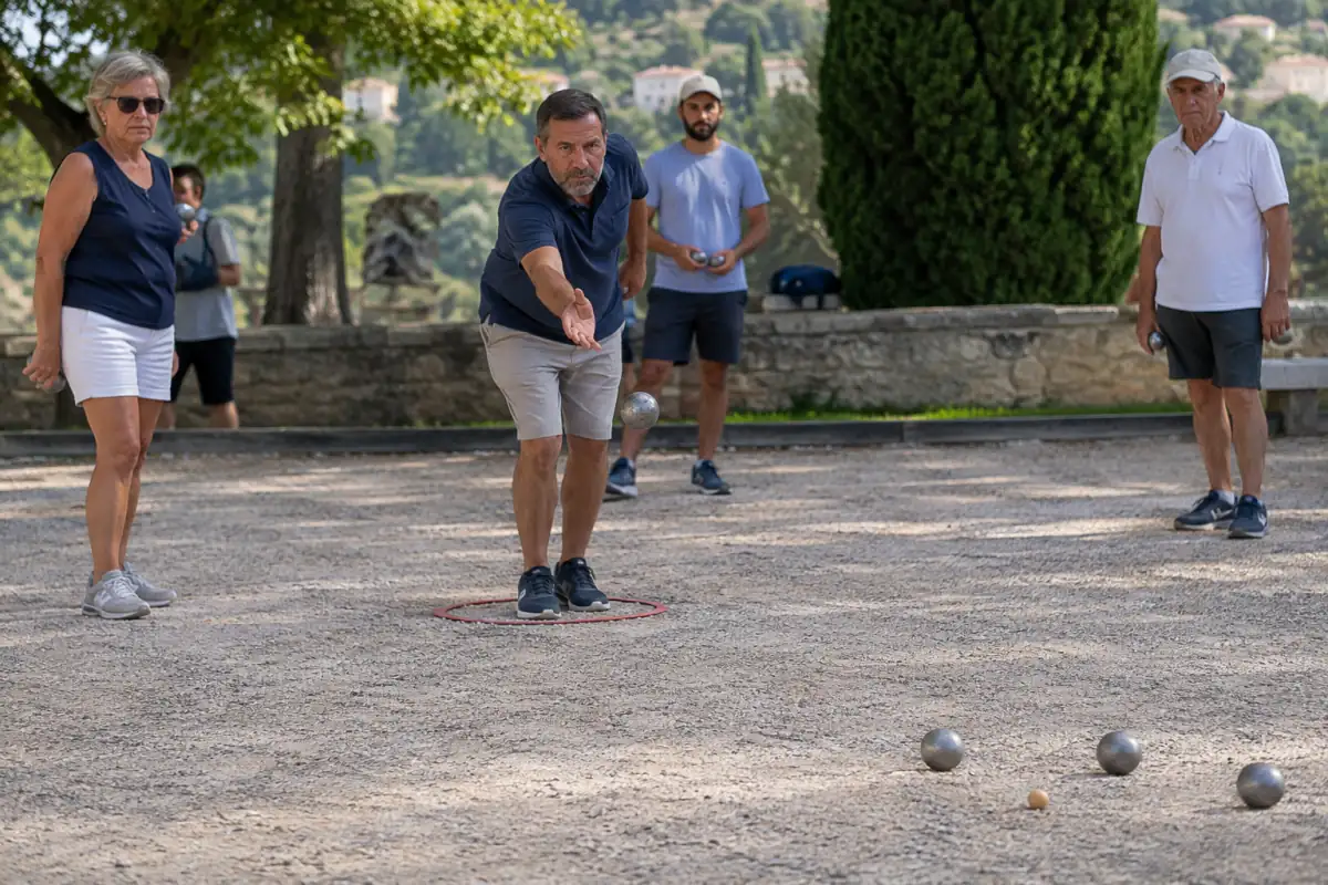 Joueur lançant une boule depuis un cercle sur un terrain de gravier lors d’une partie de pétanque.