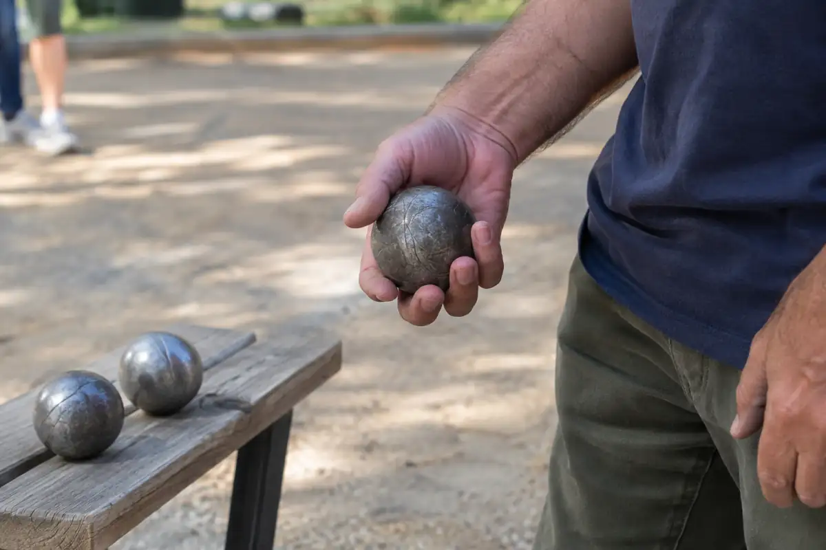 Main testant la prise d’une boule de pétanque en acier, avec deux modèles de diamètres différents posés sur un banc.