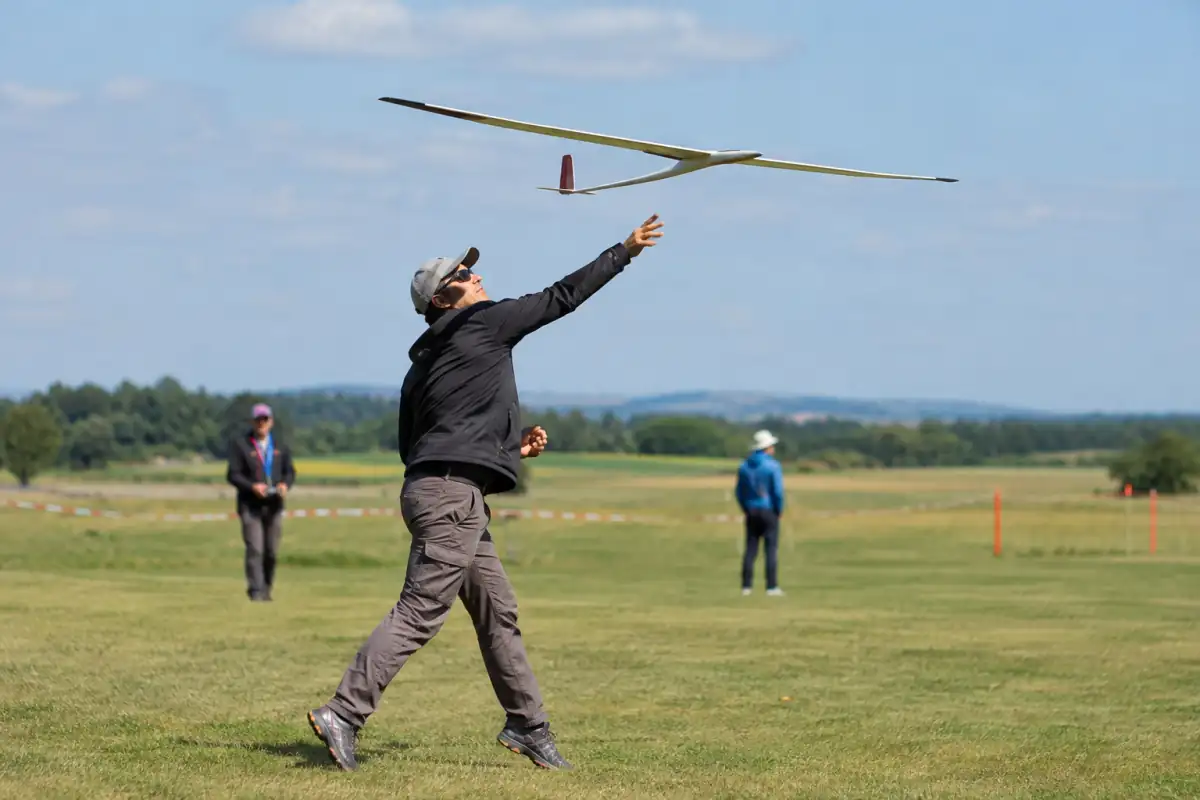 Un pilote lance à la main un planeur radiocommandé F3K sur un terrain dégagé lors d’une épreuve de compétition.