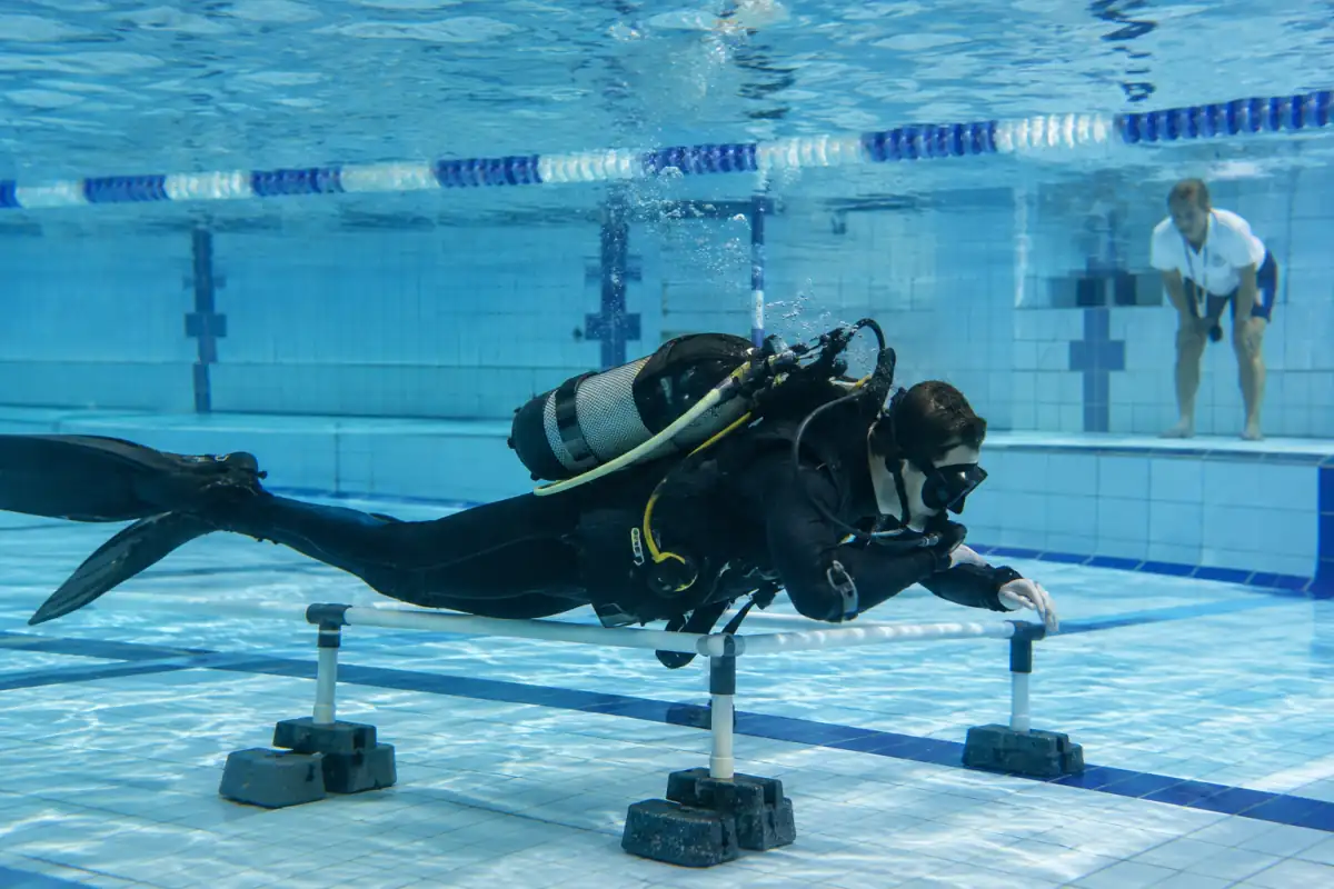 Concurrent en plongée sportive en piscine franchissant un obstacle sous l’eau avec palmes, masque et bouteille de plongée.