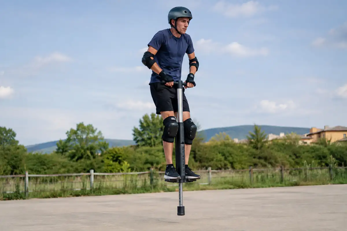 Athlète équipé d’un casque et de protections réalisant un saut contrôlé en pogo extrême sur une aire dégagée.