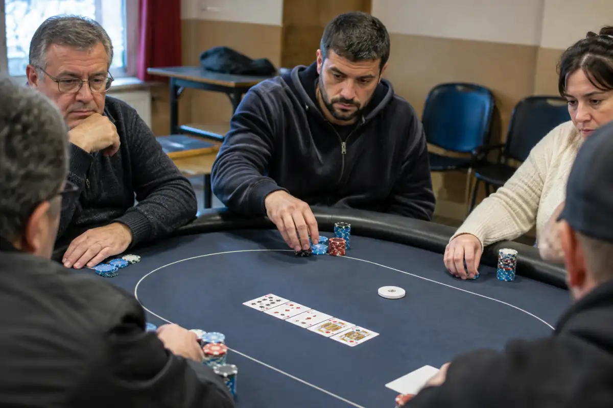 Joueurs adultes autour d’une table de poker de compétition, avec jetons de tournoi, bouton dealer et cartes communes.