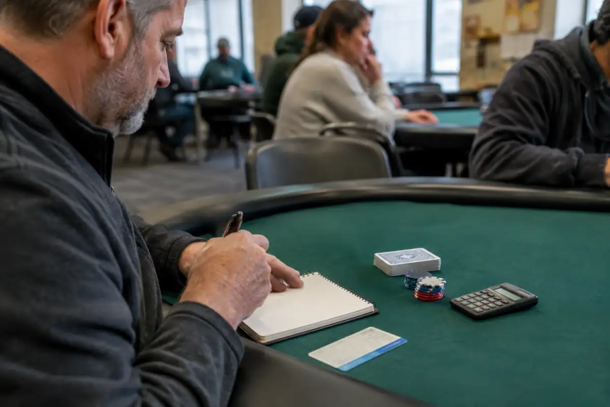 Cartes et jetons près d’un carnet de budget et d’un titre de transport, préparés avant un tournoi de poker amateur.