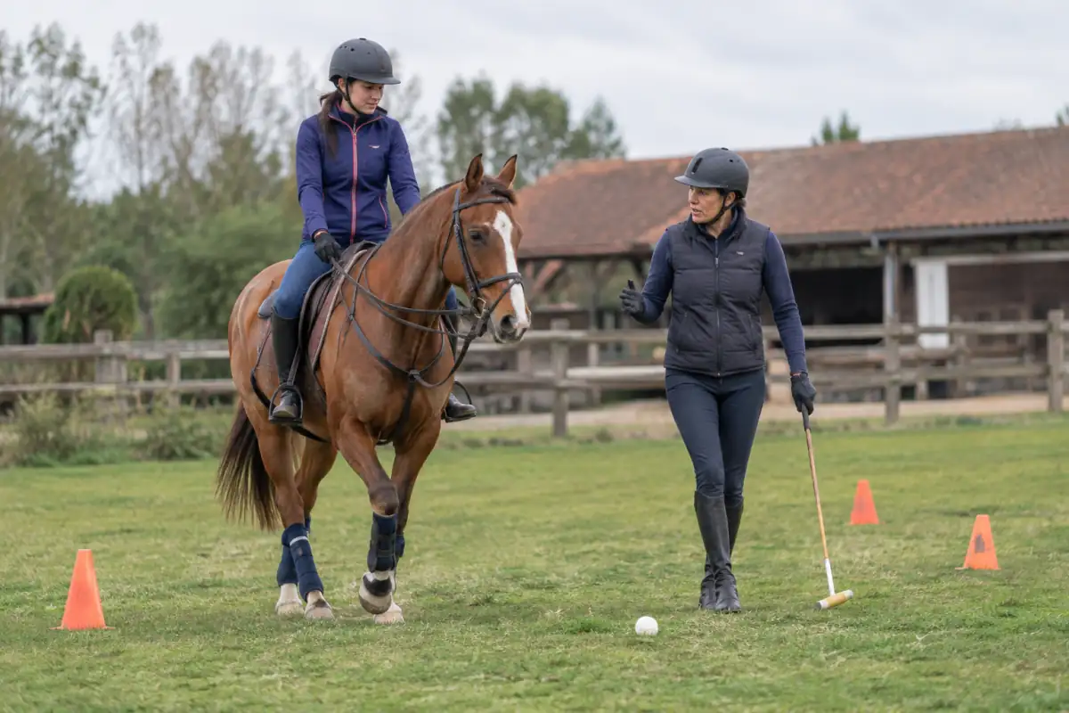 Un débutant à cheval découvre le maillet lors d’une séance de polo encadrée sur une aire d’entraînement.