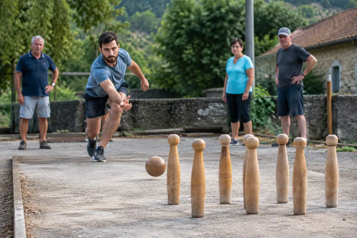 Un joueur lance une boule vers six quilles en bois sur une aire extérieure lors d’une partie de quilles de six.